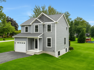 Gray two-story house by Robert Ace Builders with garage on lush green lawn, surrounded by trees and blue sky. Peaceful suburban setting.