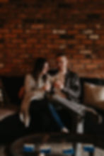 Couple sharing champagne toast on couch at home. Photographed by Nicole Leanne Photography.