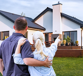 Couple on lawn, looking at a modern home, considering roofing services for their residence.