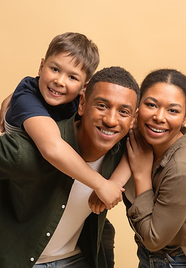 A smiling family of three poses together against a beige background, highlighting the importance of adolescent mental health as their child sits on the man's back and all look happily at the camera.