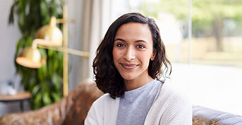 A person with shoulder-length dark hair sits indoors near a window, wearing a light-colored top. The blurred background suggests a calm setting, ideal for individual therapy or mental health counseling.