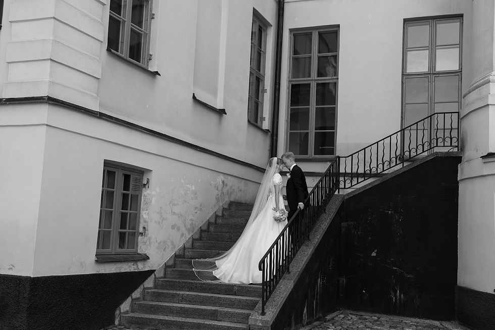 Svartvit bröllopsfotografering utanför herrgård. Brudparet står i en trappa. Bild tagen av Fotograf Cassandra J.