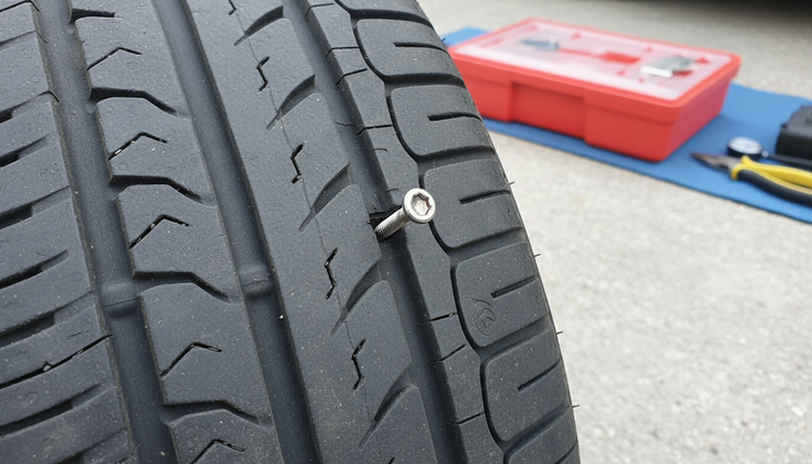 Close-up view of a screw lodged in the tread of a car tire on pavement