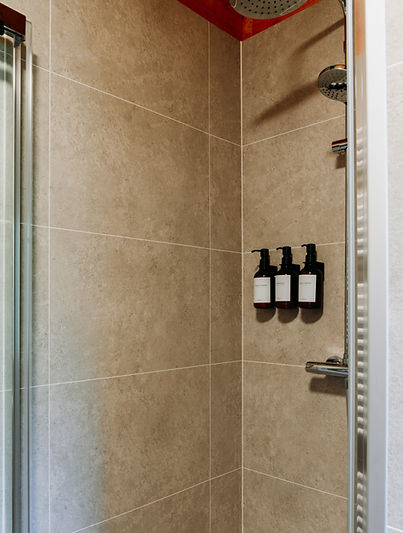 Drie stijlvolle amberkleurige wandflacons met verzorgende douchegel, shampoo en conditioner in de ruime inloopdouche