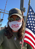 Female wearing a camouflage hat holding a US flag wearing a face mask that reads, "Stay in the Fight."
