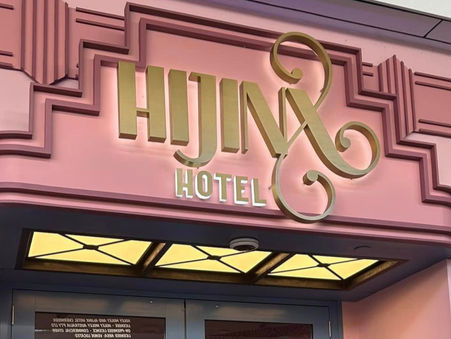 Art Deco-inspired hotel entrance with pink facade and blue doors. "HIJINX HOTEL" sign in gold above.