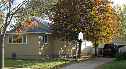 A tan house featuring a basketball hoop in the driveway.