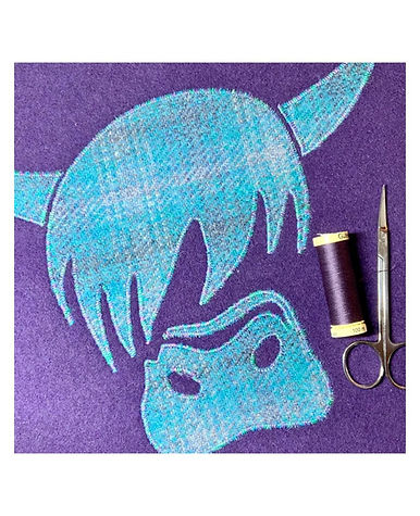 Fabric scissors and dark thread sitting on a purple fabric background with a tartan blue highland cow design on it.