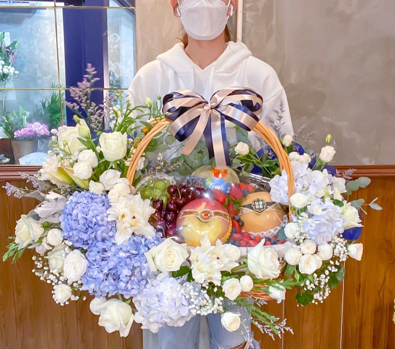 Elegant fruit and floral basket with white roses, blue hydrangeas, and premium fresh fruits, beautifully arranged