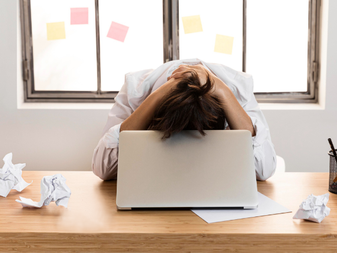 A frustrated woman behind her laptop holding her head in her hands.