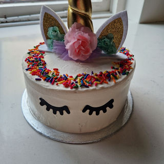 Vegan vanilla unicorn cake with horn, ears, closed eyes, and rainbow sprinkles on vanilla cream
