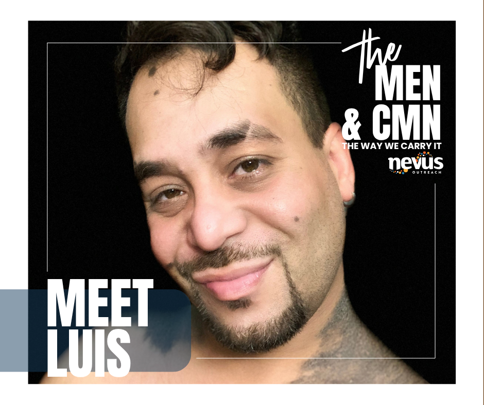 A man smiles at the camera, against a black background. He has a goatee and is proudly displaying his GCMN that wraps around the back of his neck, down his shoulders and onto his chest. On his face, it is lightly speckled with smaller nevi. His brunette hair is gently falling against his forehead like little waves. His big brown eyes meet the camera, with kindness and pride in himself.