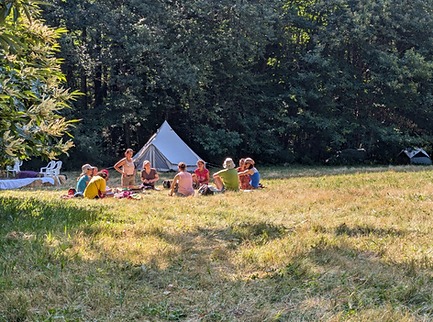 Groupe de personnes en cercle dans une prairie, entouré de forêt et d’une tente blanche, illustrant la communauté vivante et consciente.