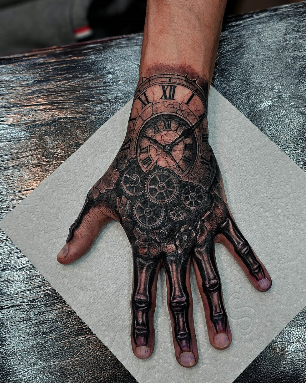 Black and grey realism hand tattoo of a clock with Roman numerals and mechanical gears