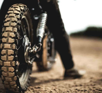 Rear view of man sitting on cafe racer motorcycle on a dusty dirt road, close up of tire..