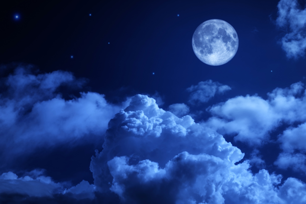 The Moon can be seen in the top right corner; the Moon is detailed with its dark spots visible. Fluffy clouds frame the Moon to its right and on the bottom half of the picture, with some wispier clouds in the backdrop of the fluffy clouds. There are stars surrounding the Moon where there are no clouds and the whole image has a blue hue.
