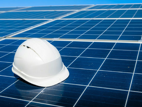 White hard hat resting on blue solar panels under clear sky, suggesting renewable energy and construction work