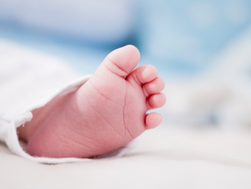 Close-up of a baby’s foot peeking from a white blanket. Soft focus background with light blue hues, creating a serene and tender mood.