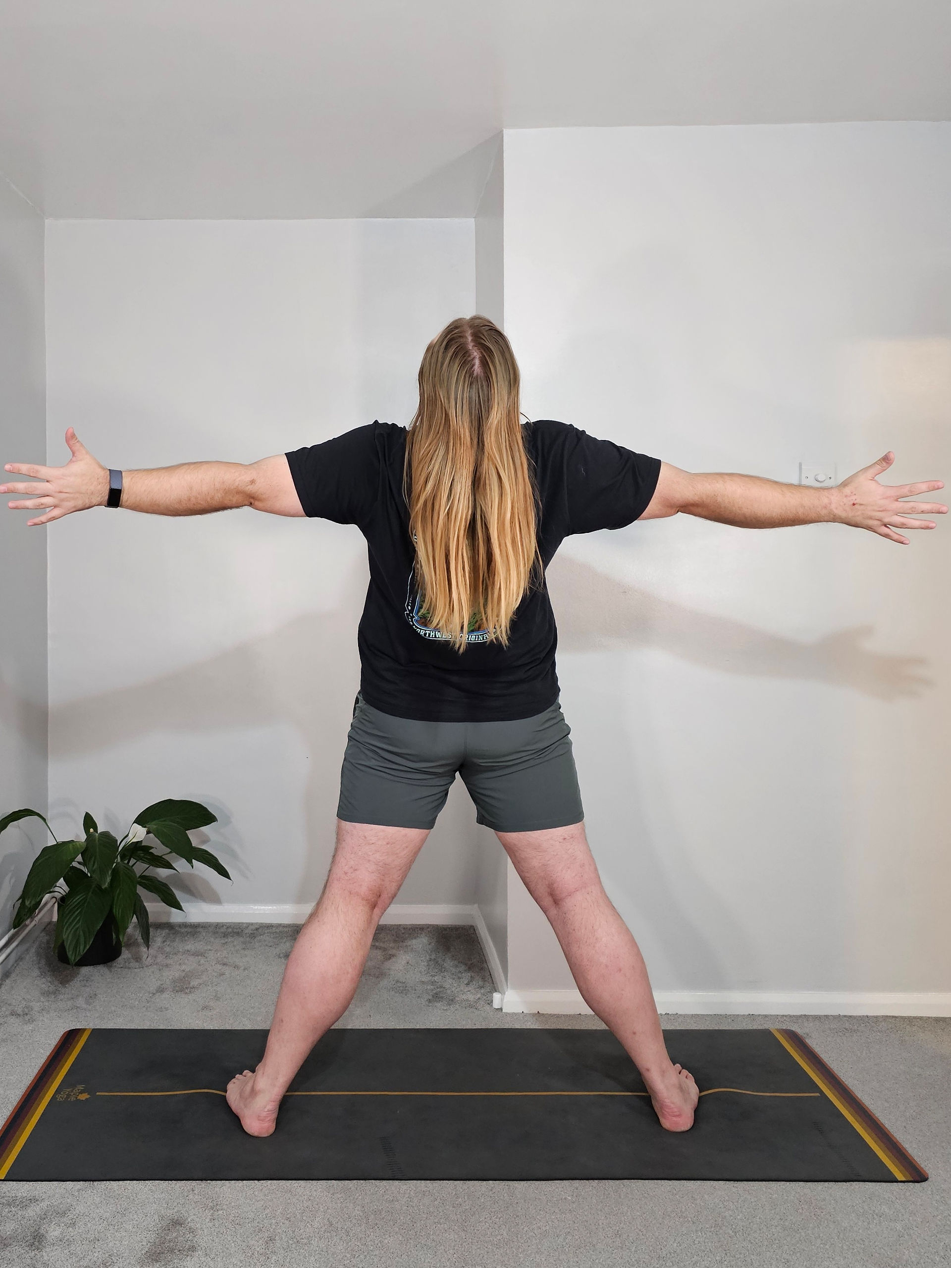 Sam Turner Yoga is stood with his feet wide part, facing towards the long edge of the mat with his arms open wide. He's trying to open the front of his body as much as possible.