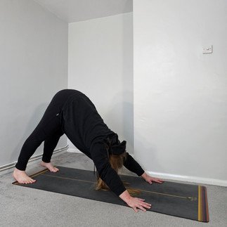 Sam Turner Yoga in downward facing dog. His hands and feet are on the ground with his bum lifted to the ceiling. His head is between his arms.