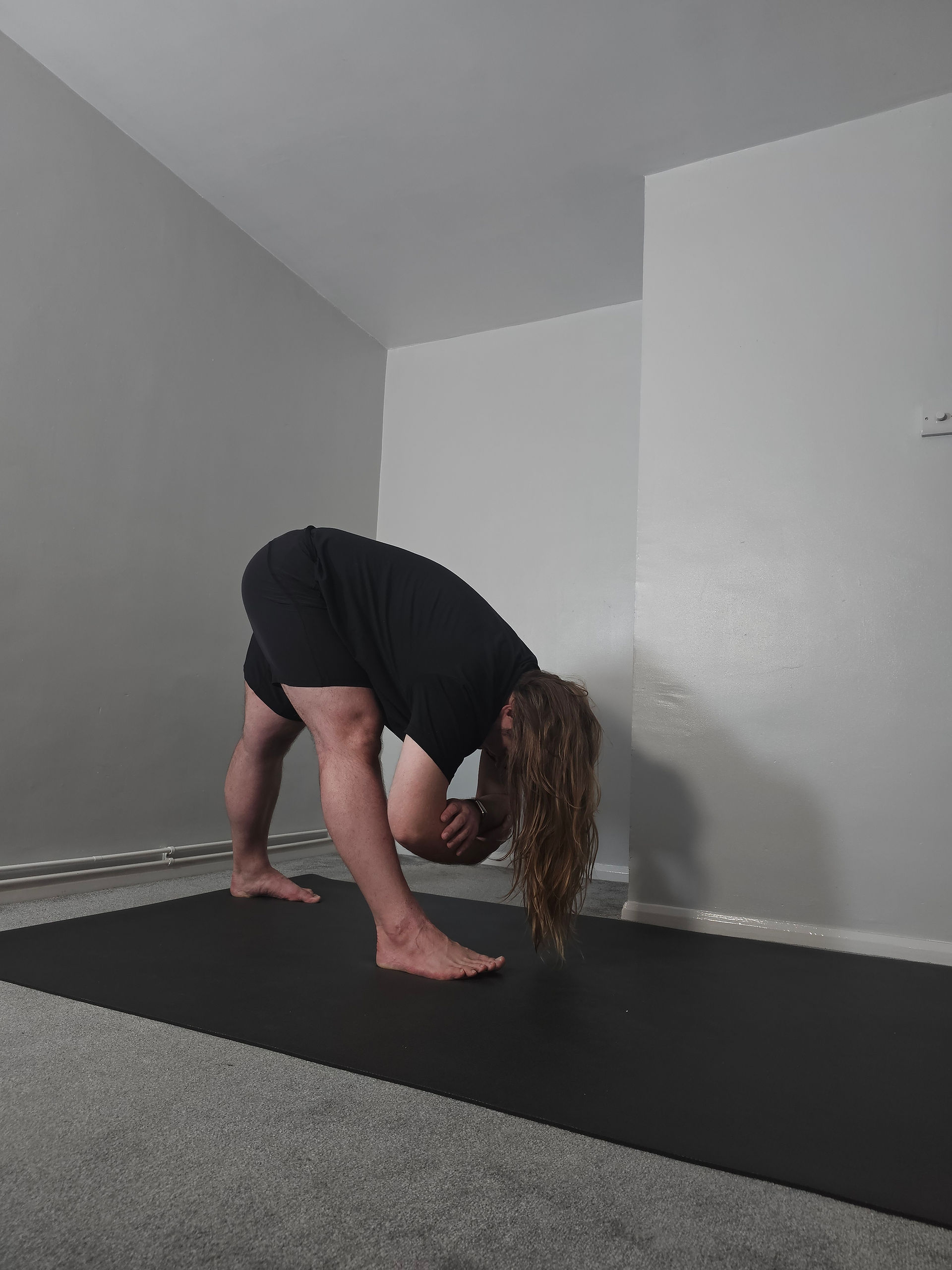 Sam standing with legs straight and staggered, torso folding forward over the front leg, with his arms dangling towards the ground.