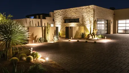 Fachada de residencia premium con iluminación exterior automatizada — jardín iluminado y acceso definido en la noche