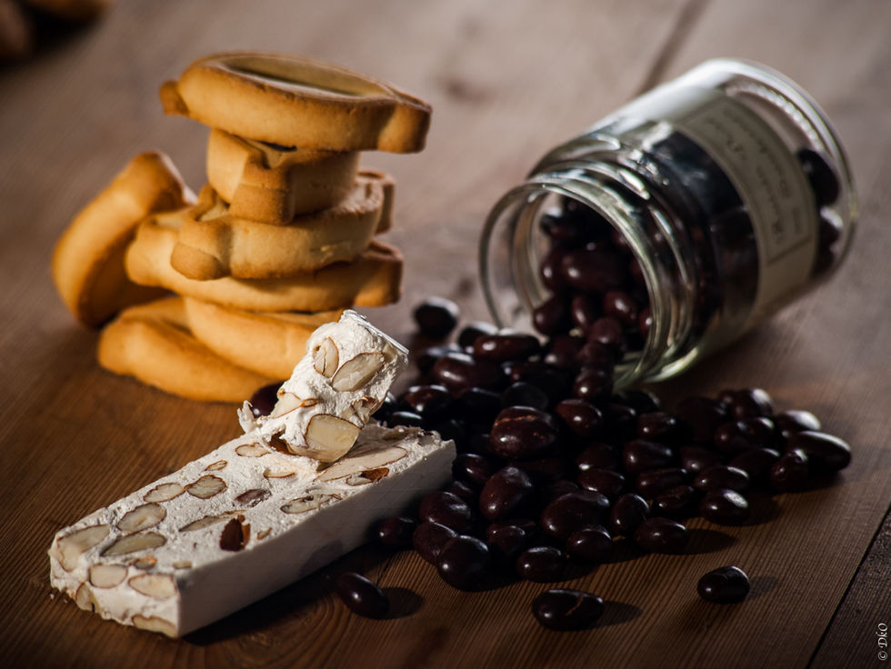 Nougat blanc rencontrant des raisins dorés (petits chocolats) sortant de leur bocal avec quelques navettes provençales en arrière plan sur une table en bois