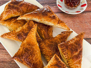 Üçgen şeklinde pofidik milföy hamuruyla hazırlanmış peynirli ve maydanozlu börek, yanında sıcak çay ile servis edilmiş