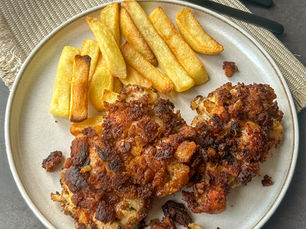 Crispy pan-fried chicken thighs coated in golden garlic breadcrumbs, served with thick-cut oven-baked fries on a ceramic plate.