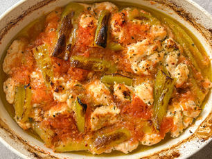Oven-baked chicken cubes with grated tomato and green peppers in a white baking dish.