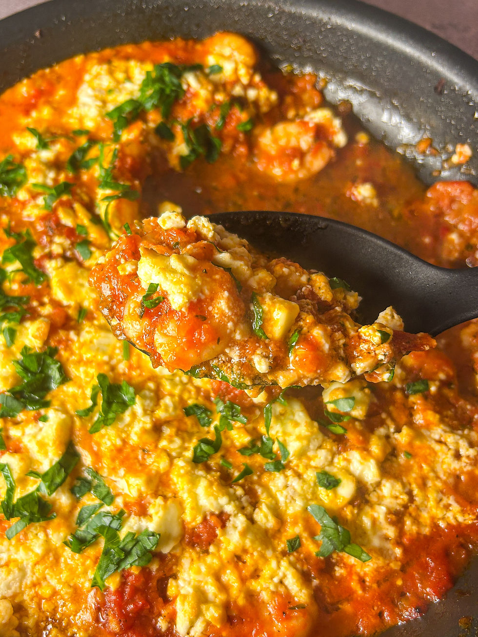 Shrimp saganaki in a black pan, spoon lifting a shrimp with tomato sauce, melted feta, and parsley on top, bright red sauce with creamy white feta.