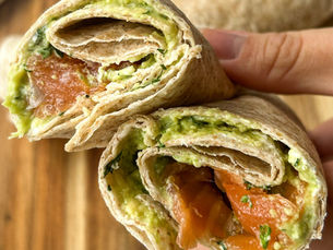 Yakından çekilmiş füme somonlu ve avokadolu wrap, krem peyniri ile hazırlanmış, ortadan kesilmiş ve iç dolgusu avokado, somon ve taze otlarla birlikte görünüyor, ahşap bir tahtada servis ediliyor.