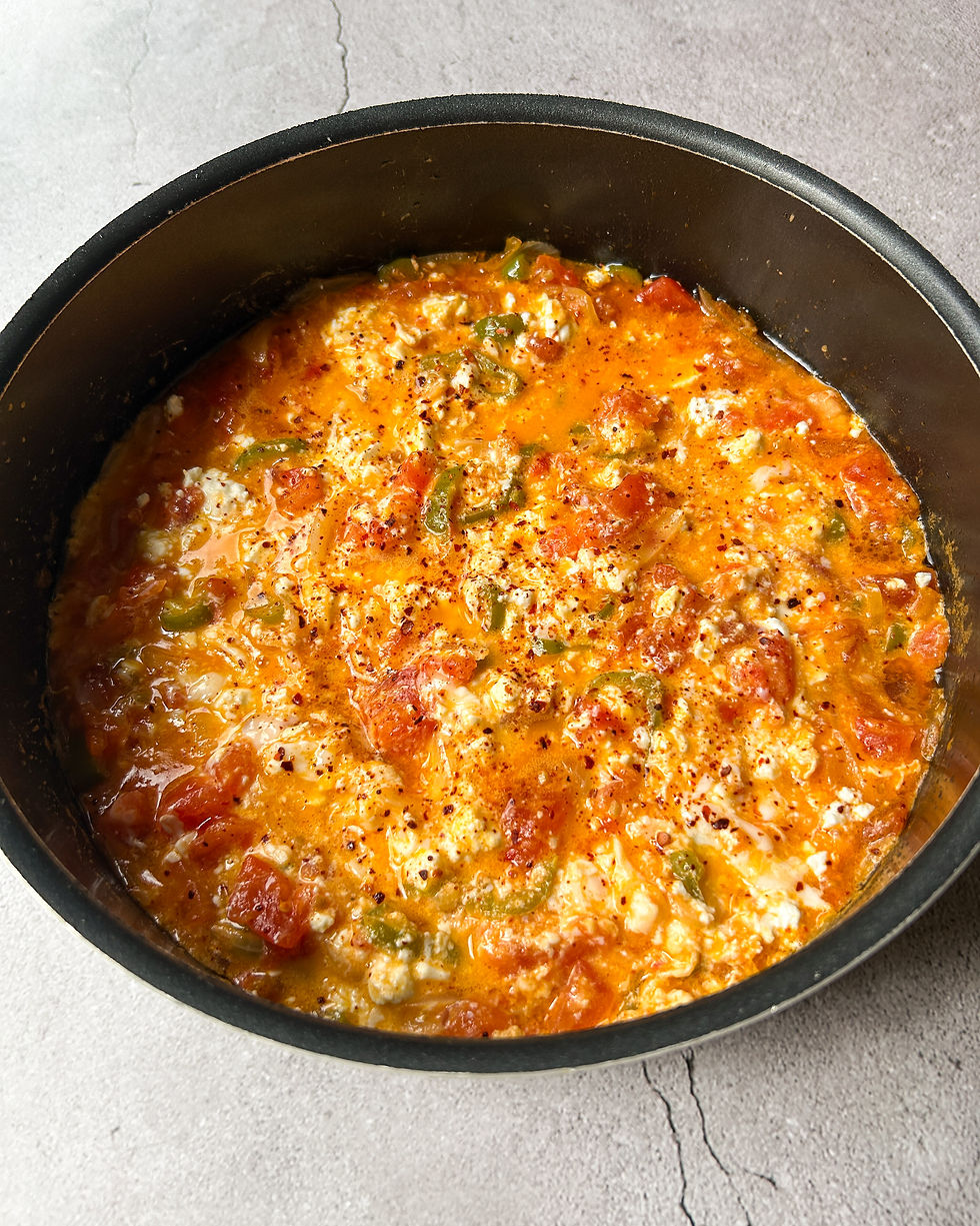 Turkish menemen in a black pan with juicy tomatoes, green peppers, and creamy scrambled eggs, topped with pul biber