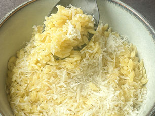 Bir kasede tereyağlı Parmesanlı arpa şehriye, üzerine taze Parmesan serpilmiş halde servis edilmiş.