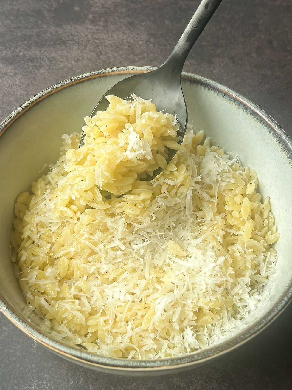 Bir kasede tereyağlı Parmesanlı arpa şehriye, üzerine taze Parmesan serpilmiş halde servis edilmiş.