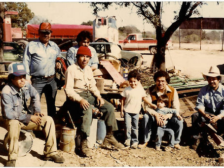 1980 photo of the Comal Iron & Metals team in New Braunfels, Texas. Johnnie Sr. next to  young Johnnie Jr. and holding Roger while employees gather in the scrap metal recycling yard.