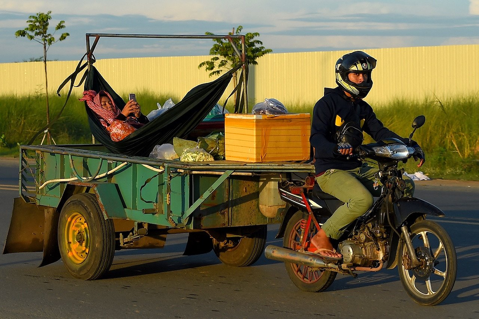A man rides a motorbike pulling a trailer with a woman relaxing in a hammock, checking her phone, on a street in Phnom Penh on June 12, 2020. / AFP / TANG CHHIN Sothy