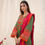 Thumbnail: A woman in a green and red embroidered giza cotton Kurta and red chanderi dupatta is posing sideways next to a small, round table with a vase of red roses against a beige backdrop.
