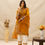 Thumbnail: female model posing in mustard muse by mukhtar sarees gul season 3 of mustard color and 100% giza cotton kurta/pant and checks organza dupatta featuring in beige background with abstratc flowers adding to the summer vibe