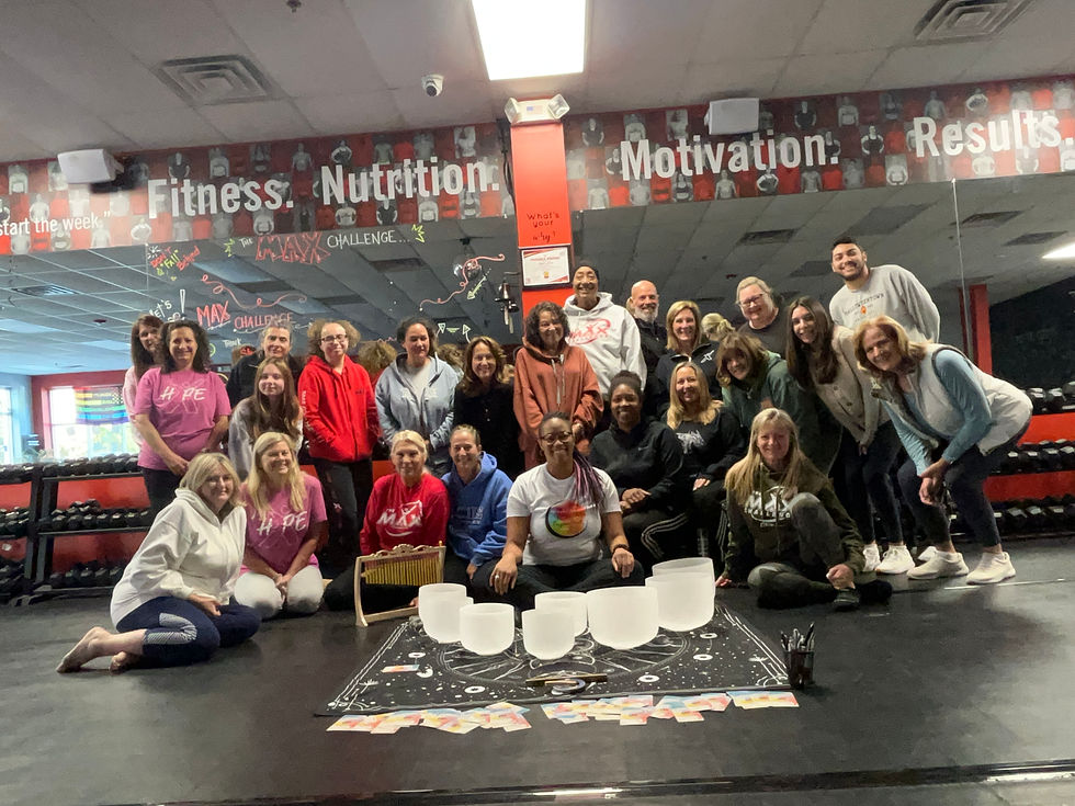 Group of people posing and smiling in a gym with text "Fitness. Nutrition. Motivation." on mirrored wall. Bowls and cards on floor.