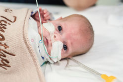 perth-birth-photographer-captures-prematurely-born-baby-boy-laying-on-his-back-ion-crib-with-beige-blanket-covering-him--with-his-name-on-it-being-fed-by-ng-tube-at-king-edward-memorial-hospital-perth-nicu-photography-project