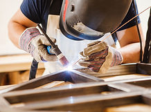 Person using a Tig welding torch and filler rod to connect a few pieces of metal, making a metal frame.