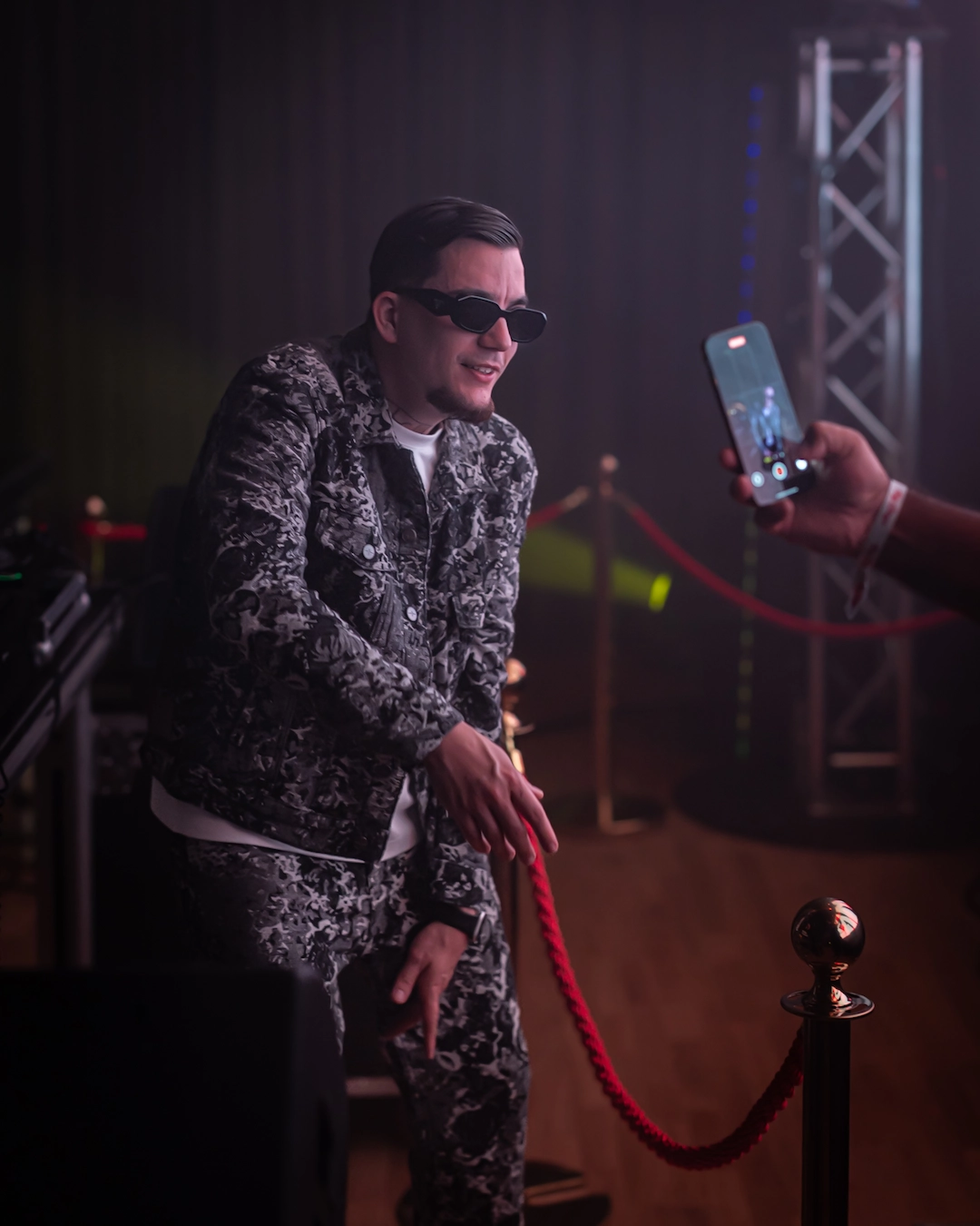 DJ interacting with the crowd near the stage at a ParisLatino event, captured under low light with stage equipment and venue barriers in the background.