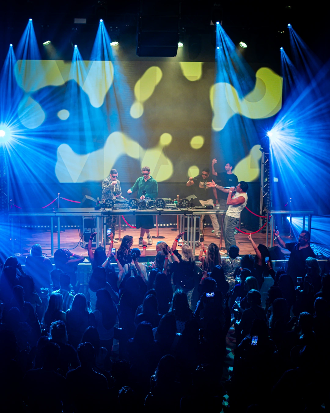 Crowd gathered in front of the stage at a ParisLatino event, with multiple DJs performing under blue stage lights and visuals at Jacy’z Big Stage in Gothenburg.