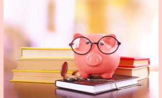 A pink piggy bank with glasses sits on books on a wooden table. The background is softly blurred, creating a warm, scholarly ambiance.