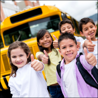 Smiling children in front of a yellow school bus show thumbs up. They wear casual clothes and backpacks. The mood is cheerful and energetic.