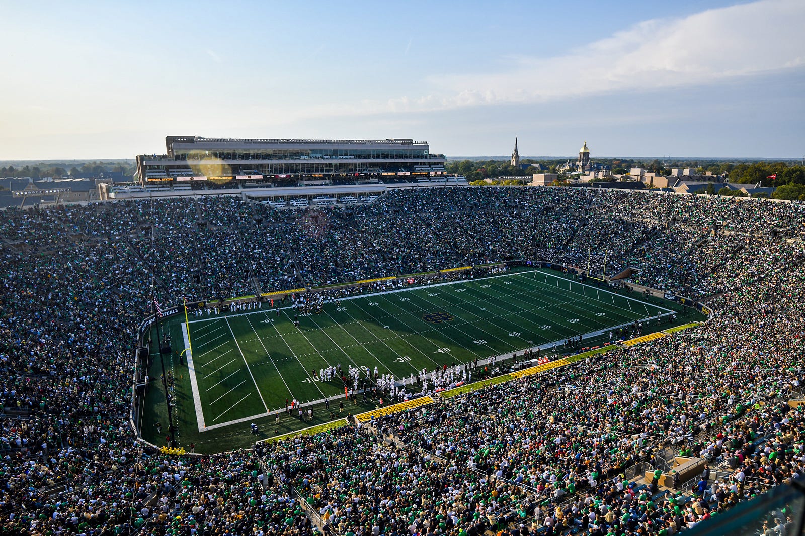 Notre Dame Stadium packed with students and fans.  Football on the sidelines.  Golden Dome in the distance.  Autobiography of Dr. Anthony J. Carbone.