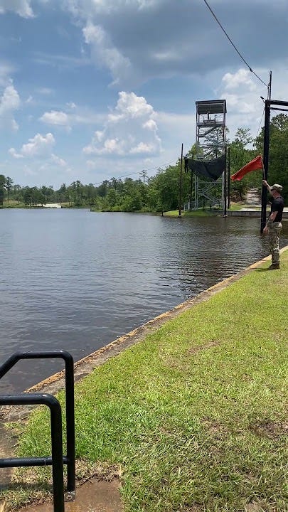 Slide for Life at U.S. Army ROTC Advanced Camp.  Instructor on bank holding a signal flag.  Slide For Life in the background.  Biography of Dr. Anthony J. Carbone.