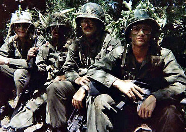 Photograph of me (in foreground) with 3 of my squad members during tactical training.  Wearing olive drab fatigues, camouflaged steel pot helmets, tactical gear and carrying our M16A1 rifles. Biography of Dr. Anthony J. Carbone