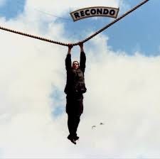 U.S. Army cadet at Recondo water obstacle area.  Hanging over water holding onto a rope with Recondo sign.  Biography of Dr. Anthony J. Carbone.